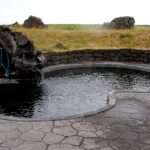 Bassin d'eau chaude à ciel ouvert entouré de dalles et de pierres, dans un paysage dégagé