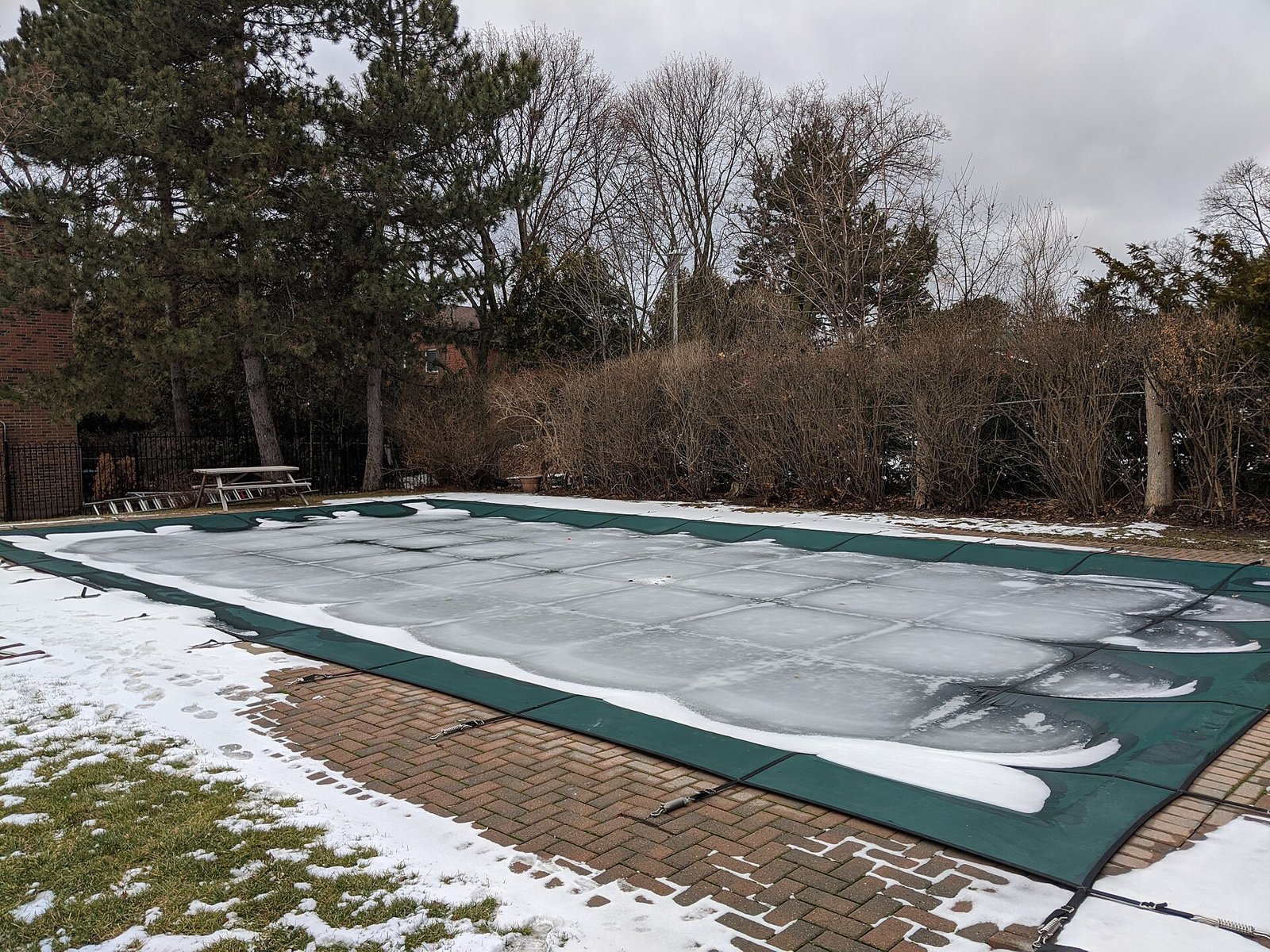 Piscine couverte d'une bâche d'hiver dans un jardin enneigé