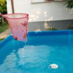 Épuisette rose tenue au-dessus d'une piscine hors-sol bleue