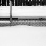 Bord de piscine et échelle sous la neige, avec la margelle et la frise de carrelage visibles